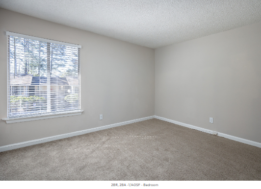 An empty bedroom with a large window and a carpeted floor.