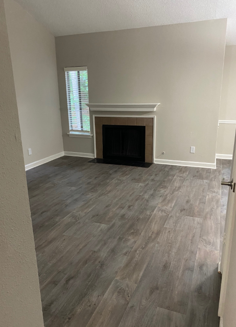 An empty living room with a fireplace and hardwood floors.