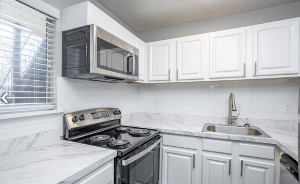 A kitchen with a stove , microwave , sink and white cabinets.