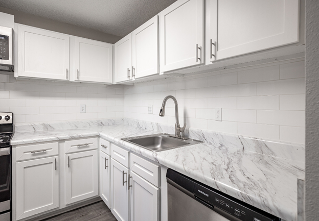 A kitchen with white cabinets , stainless steel appliances , marble counter tops and a sink.