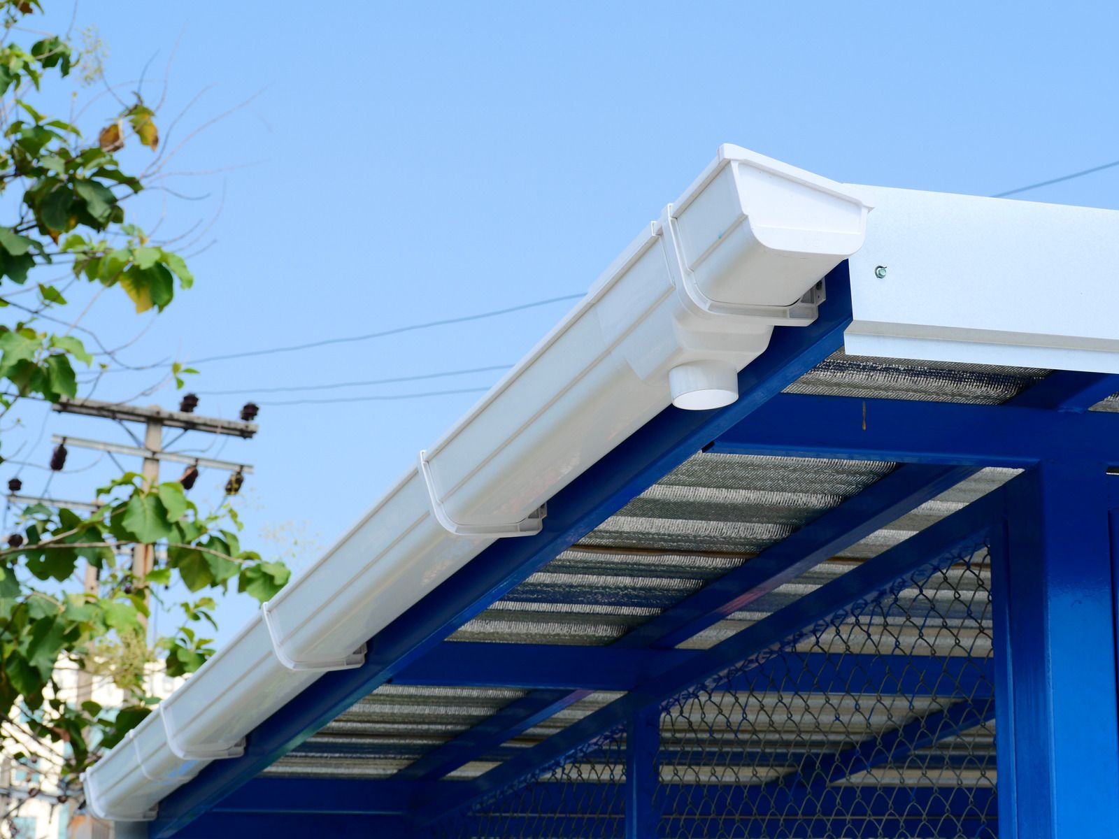 White gutters along the edge of a blue metal-framed structure with a metal roof, against a blue sky.
