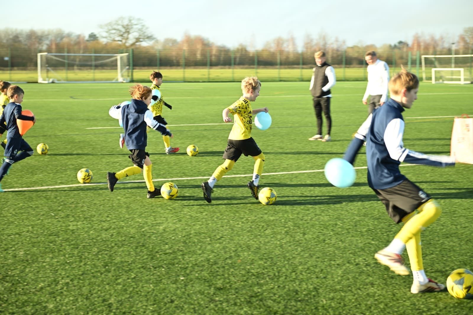 Children in yellow and blue soccer uniforms practice drills on a green field.