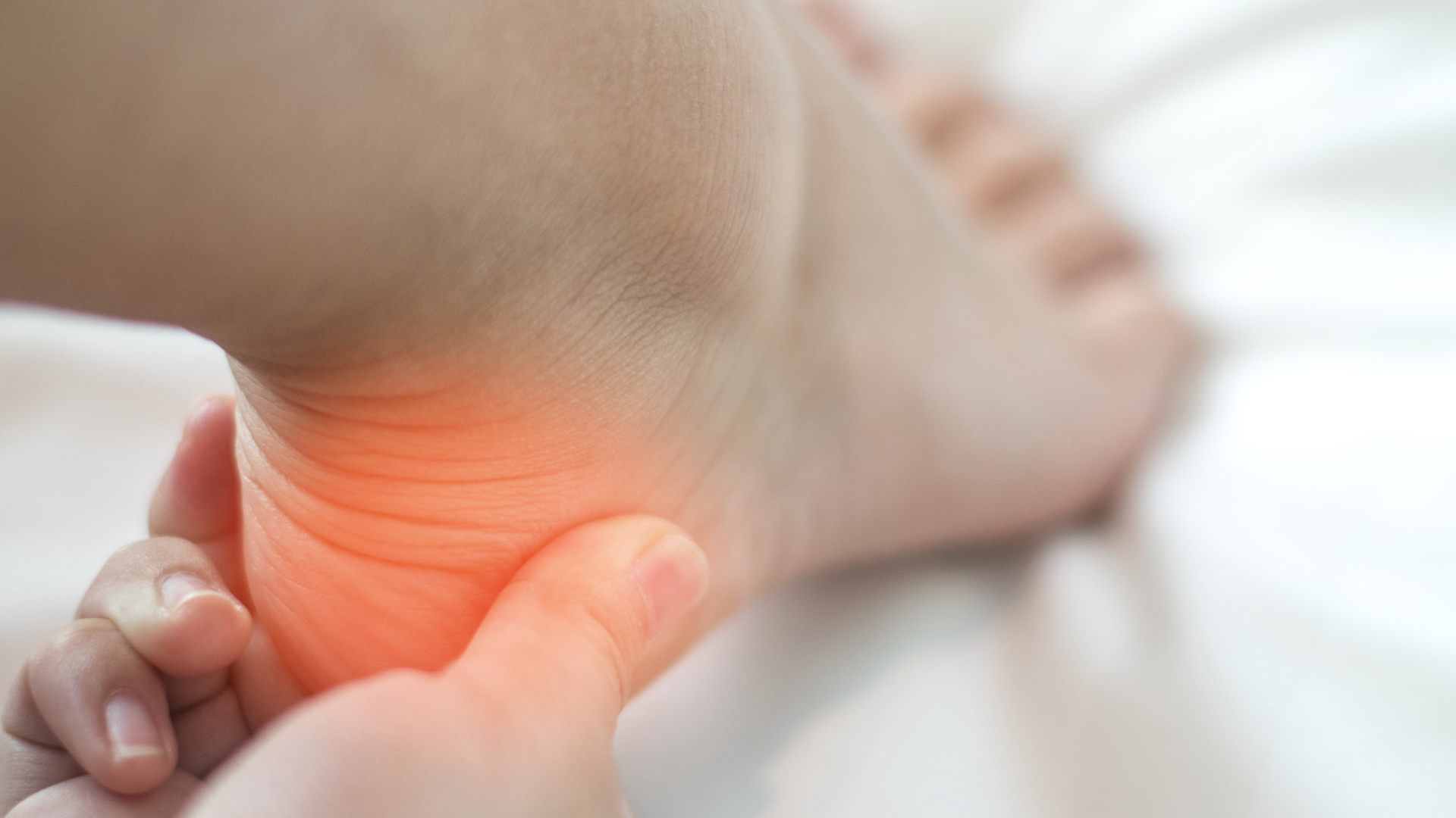 Person holding their heel, highlighting a red, painful area.