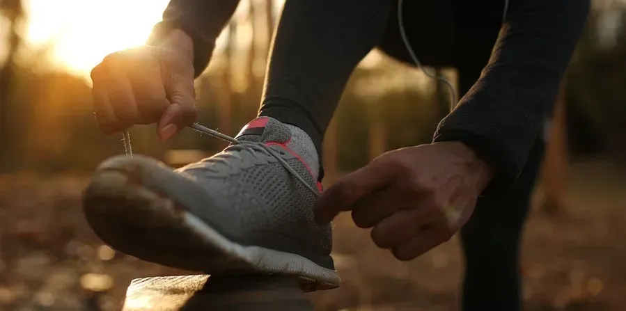 Person tying their running shoe outdoors in the sunlight.