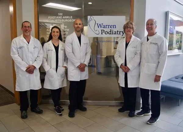 Five medical professionals in white coats stand in front of a clinic entrance, labeled 