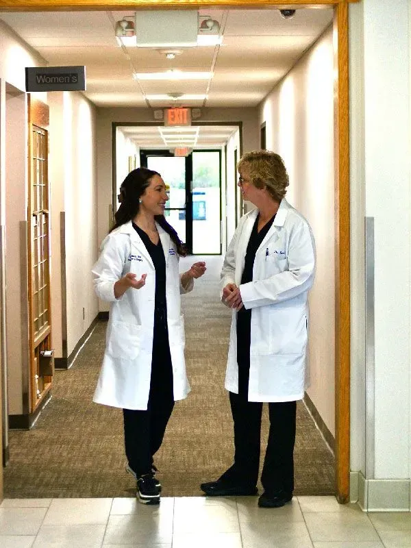 Two people in white coats converse in a hospital hallway.