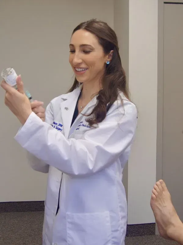 Doctor in white coat holding syringe, smiling, preparing to inject a patient's foot.