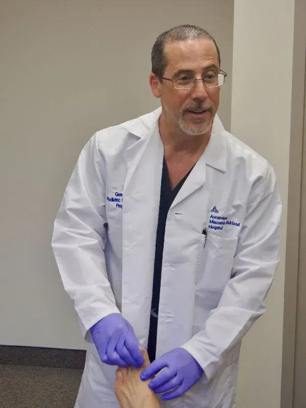 Doctor in white coat examining a foot, wearing gloves, in a hospital setting.
