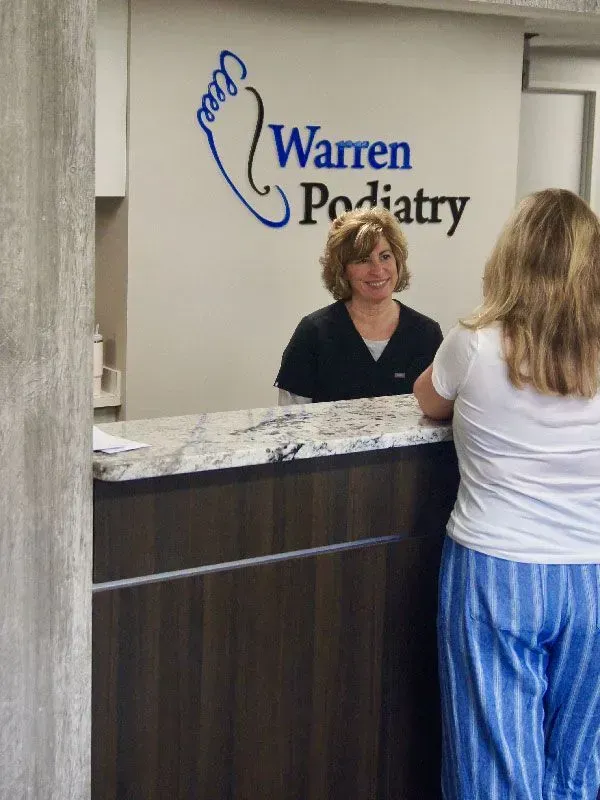 Receptionist at the Warren Podiatry office assisting a patient. Sign and logo visible.