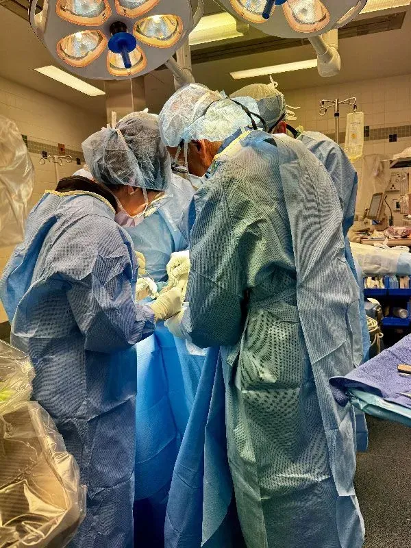 Medical staff in blue scrubs and caps perform surgery in an operating room.