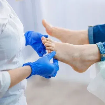 A medical professional wearing blue gloves examines a patient's foot.
