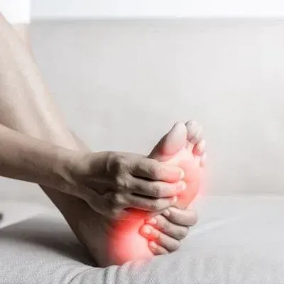 Person's hand gripping foot, indicated with a red spot on the sole, possibly due to pain or injury.