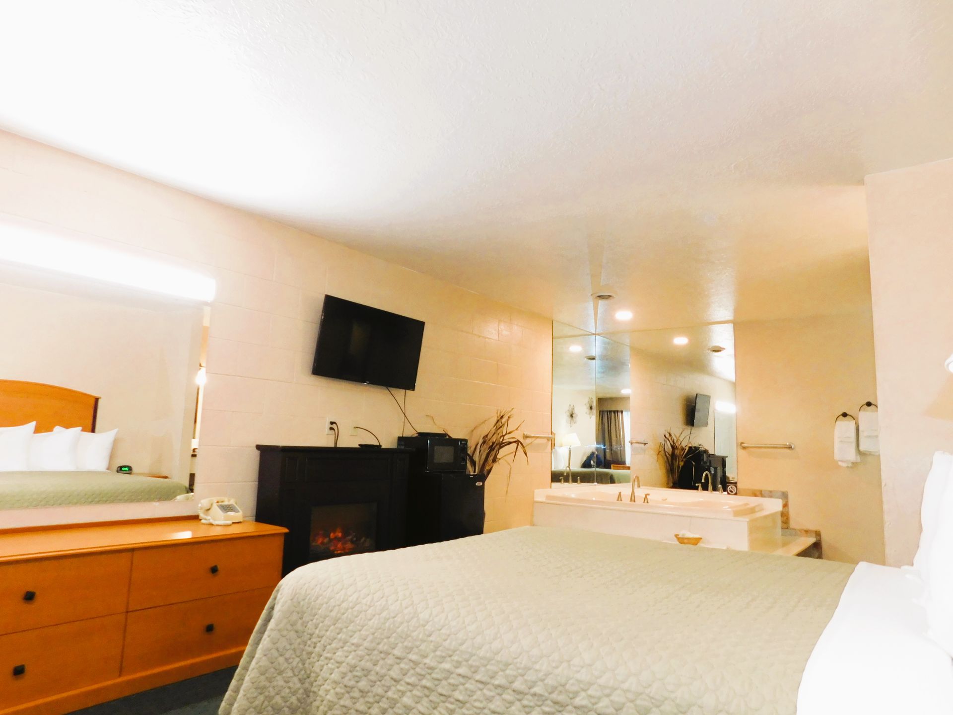 Hotel room with bed, dresser, fireplace, TV, and jacuzzi.