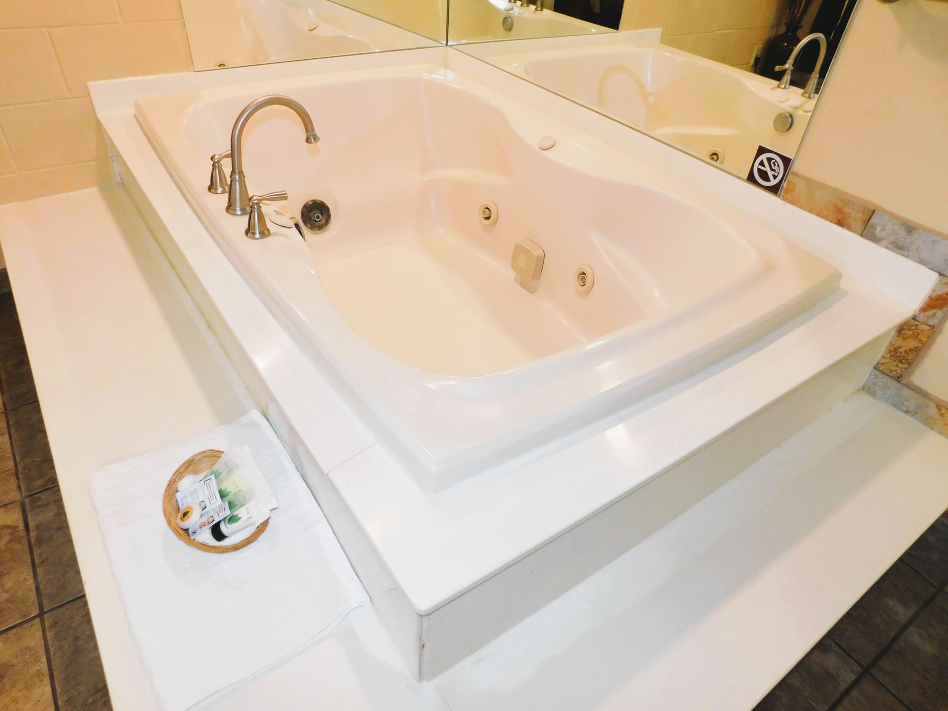 White bathtub inside a raised white platform with a faucet and jets. A small basket with flowers sits nearby.