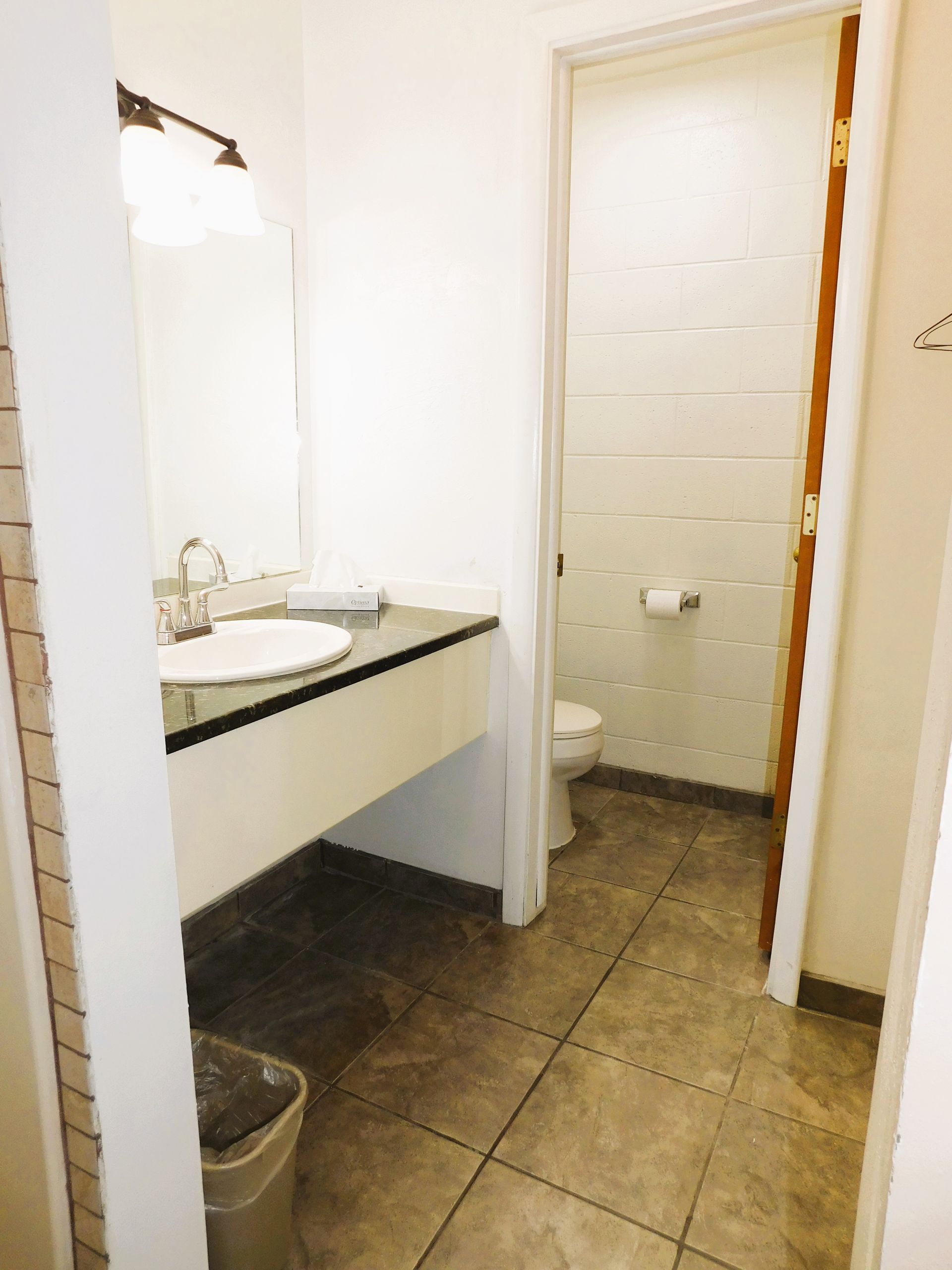 Bathroom with sink and toilet. White walls, tile floor, open door.