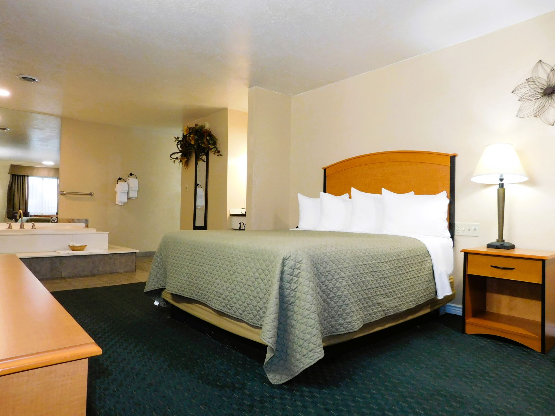 Hotel room with bed, nightstand, and jacuzzi tub. Green carpet, tan walls, and wooden furniture.