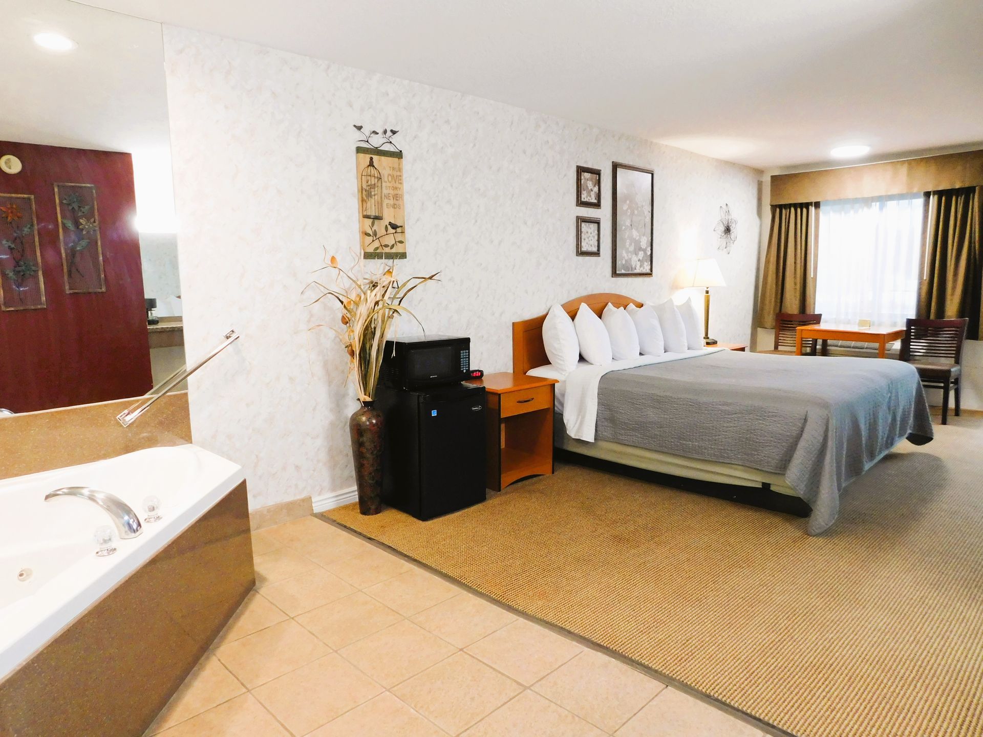 Hotel room with king bed, jacuzzi, microwave, and small table. Beige carpet and white walls.