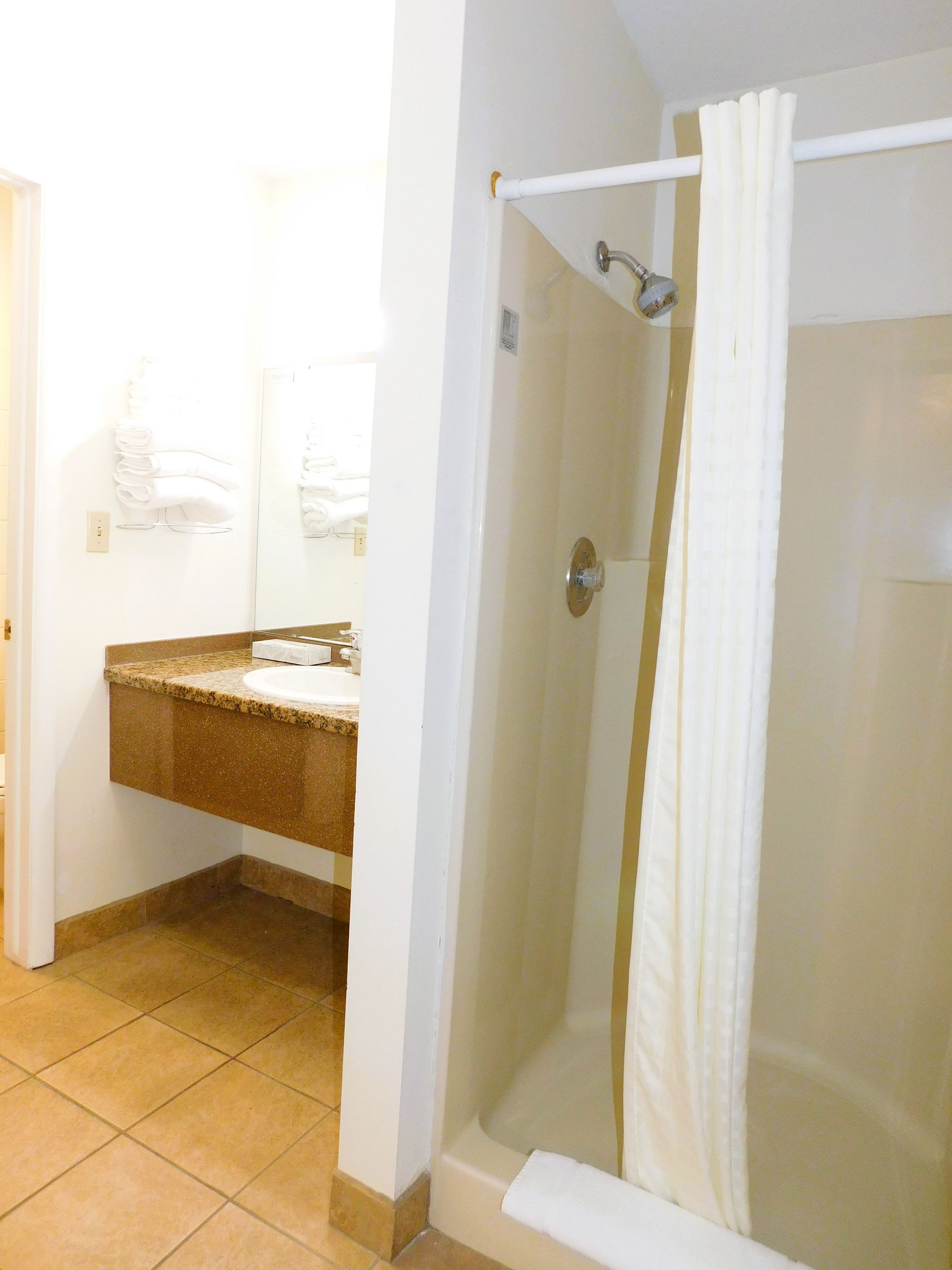 Bathroom with shower, vanity, and tan tile floor. Beige shower curtain and walls.