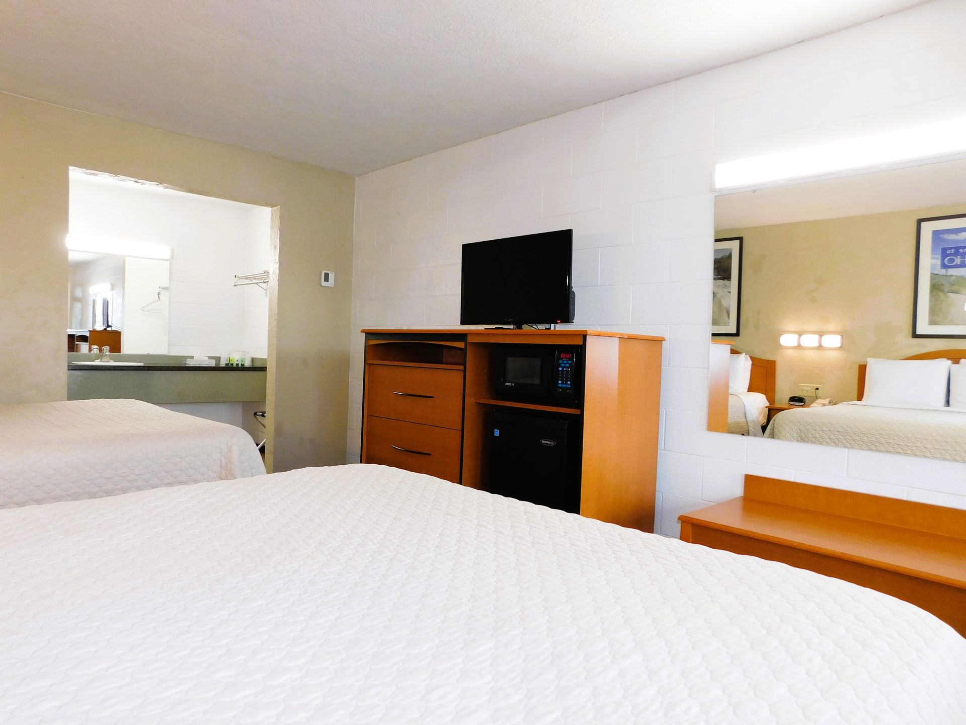 Hotel room with two beds, TV, microwave, dresser, and bathroom visible in the background.
