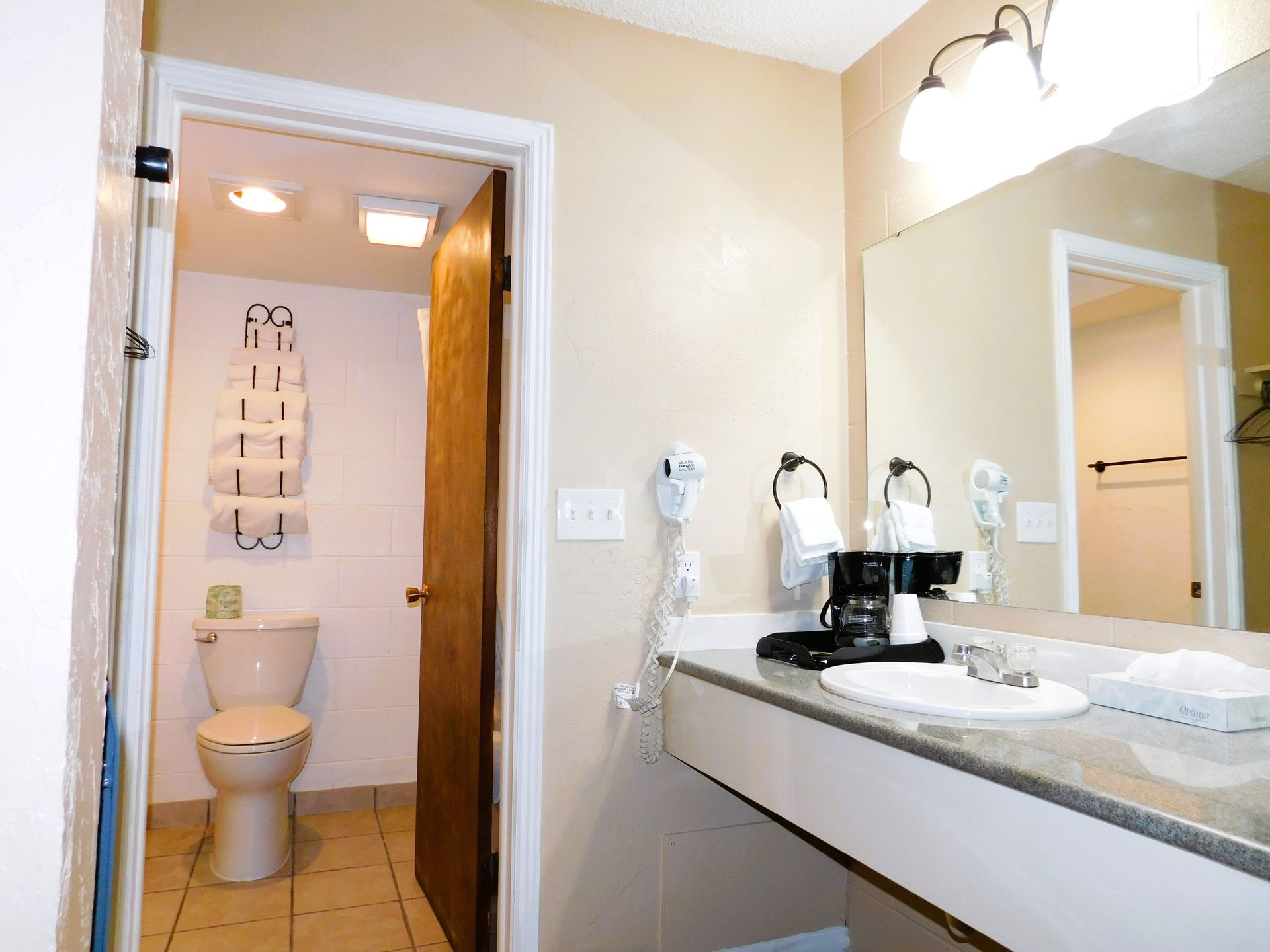 Bathroom with a vanity, mirror, and a doorway to a toilet and towel rack.
