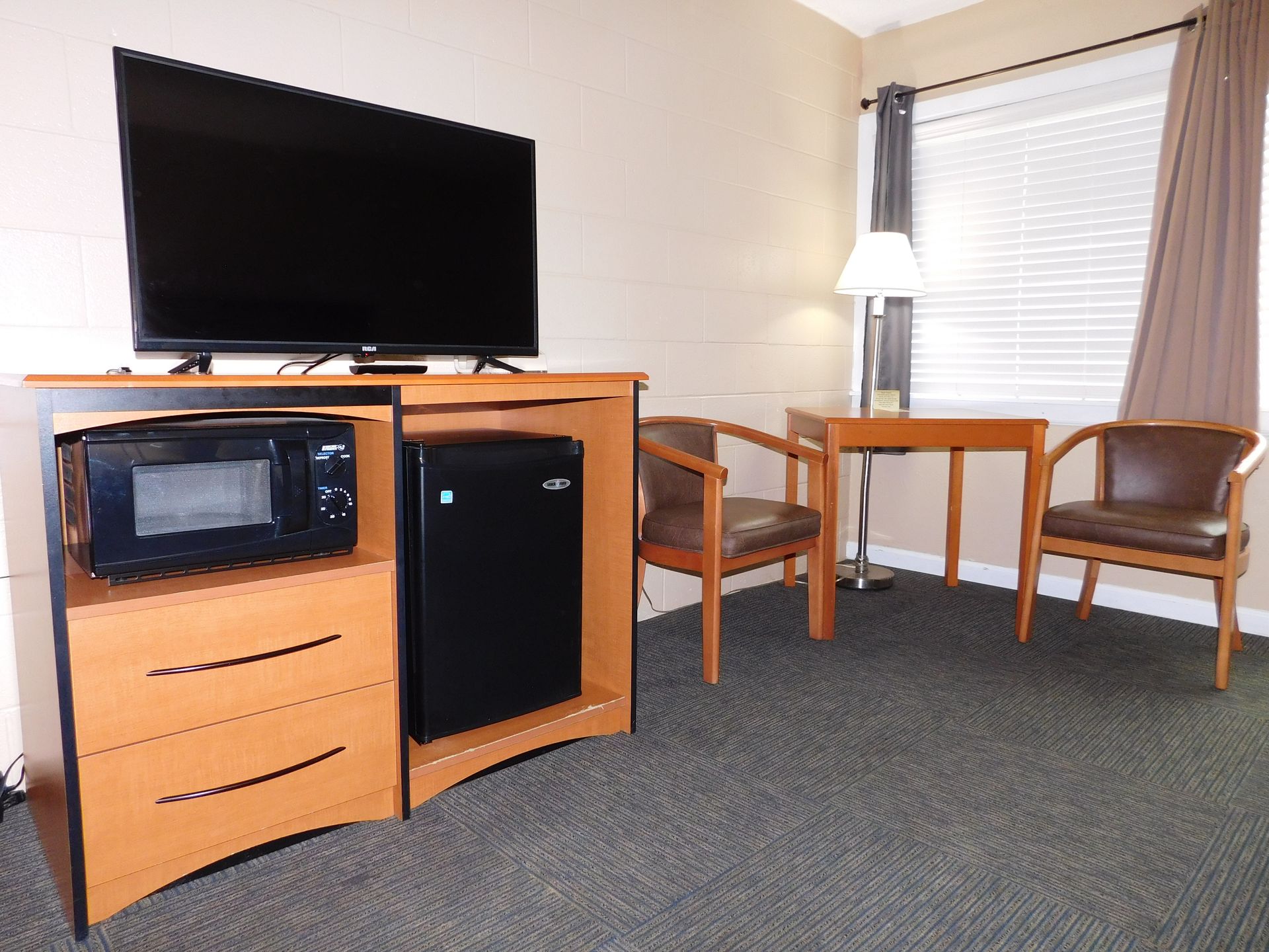 Hotel room with a TV, mini-fridge, microwave, desk, chairs, and window.