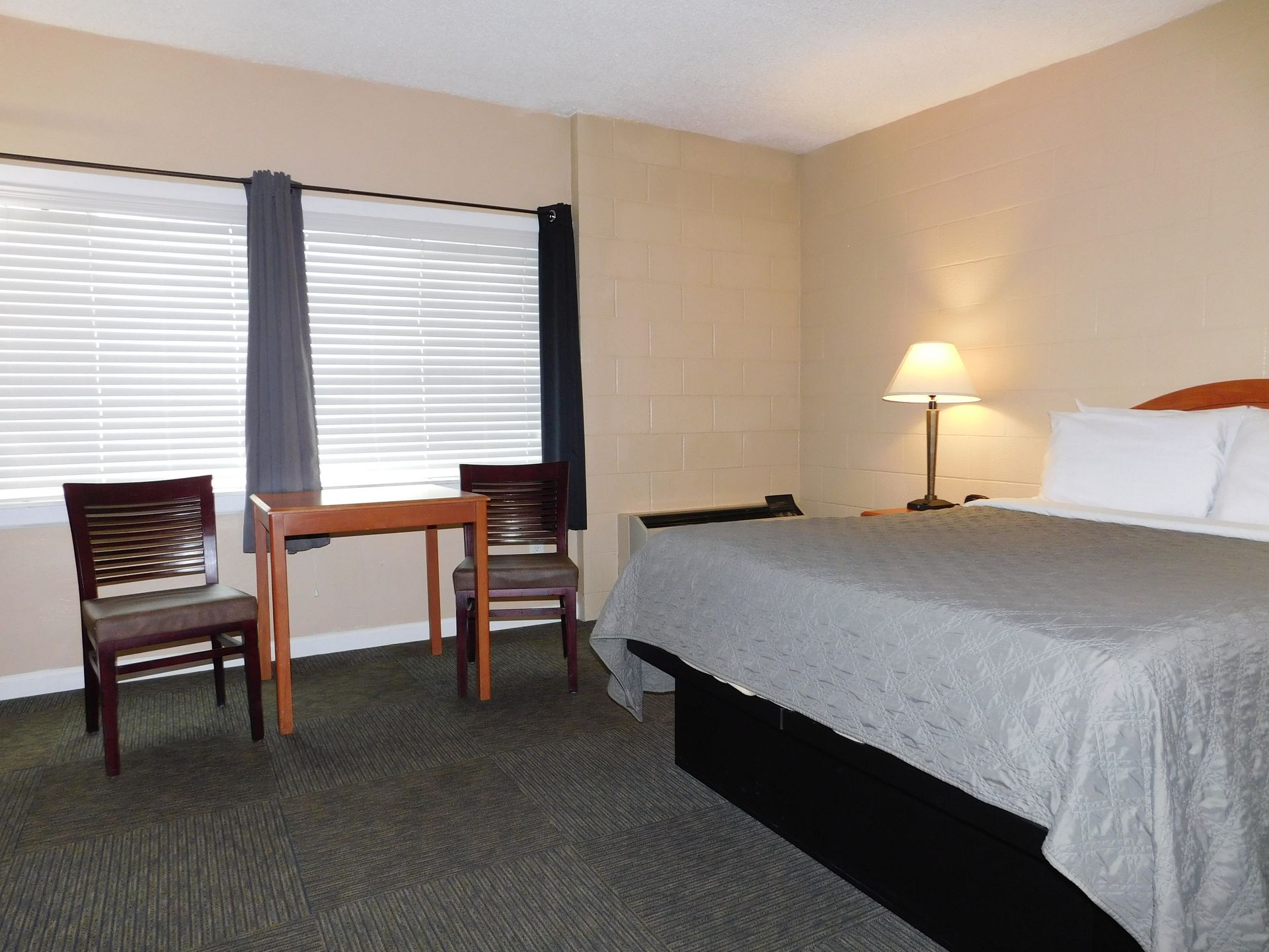 Hotel room with bed, table, chairs, window, and lamp.