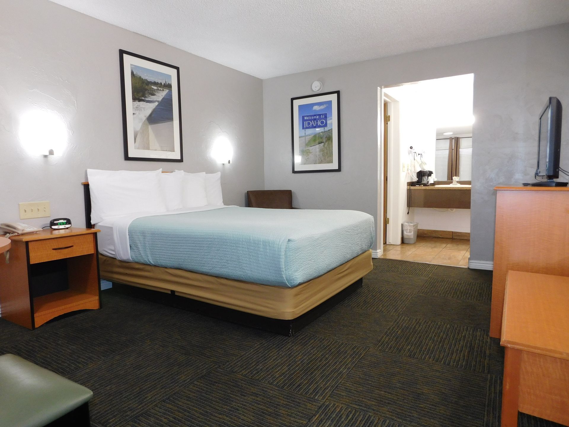 Hotel room with a bed, nightstand, television, and bathroom entrance.