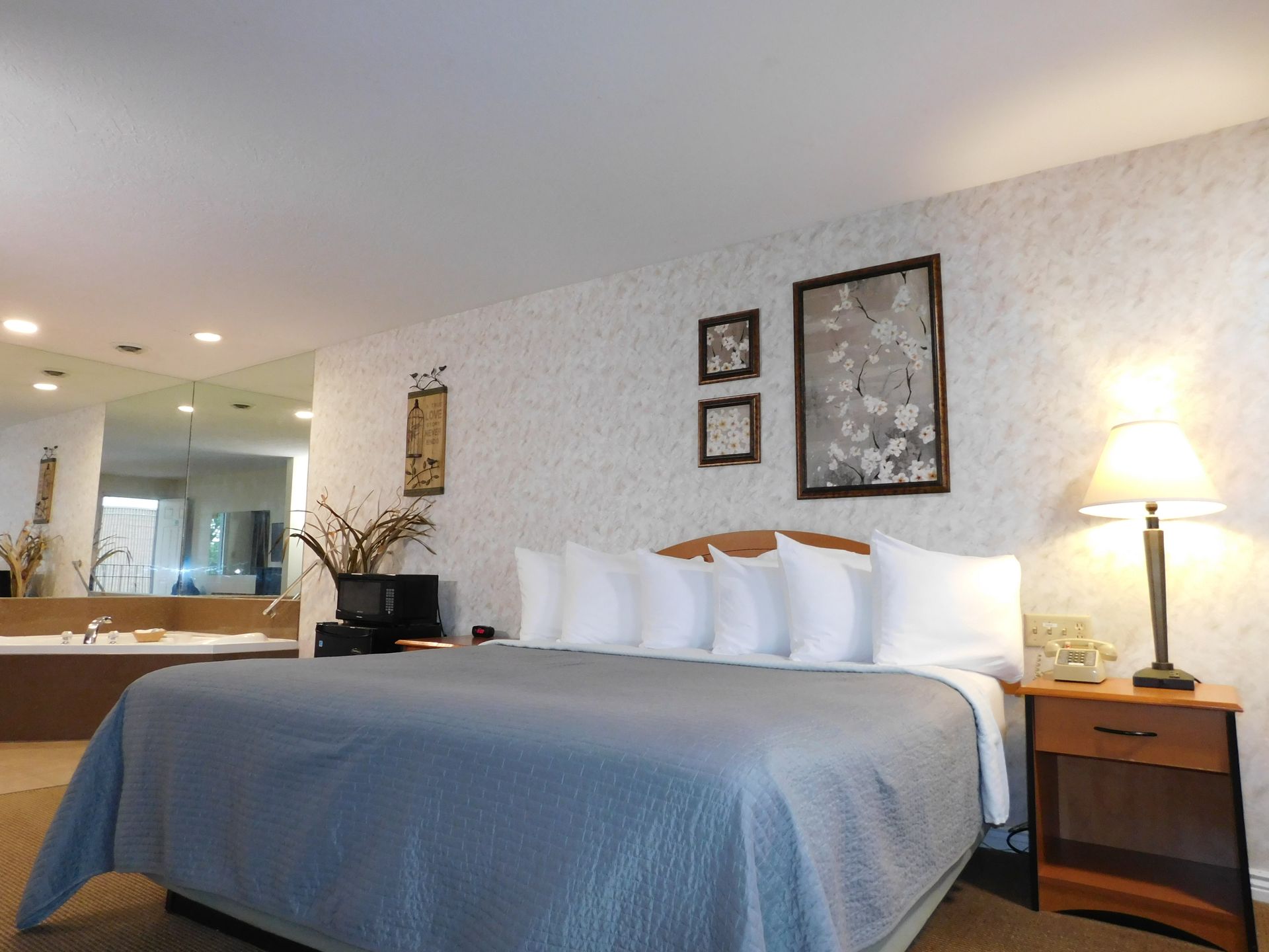 Bedroom with bed, nightstand, and jacuzzi visible. Soft colors, framed art on the wall.