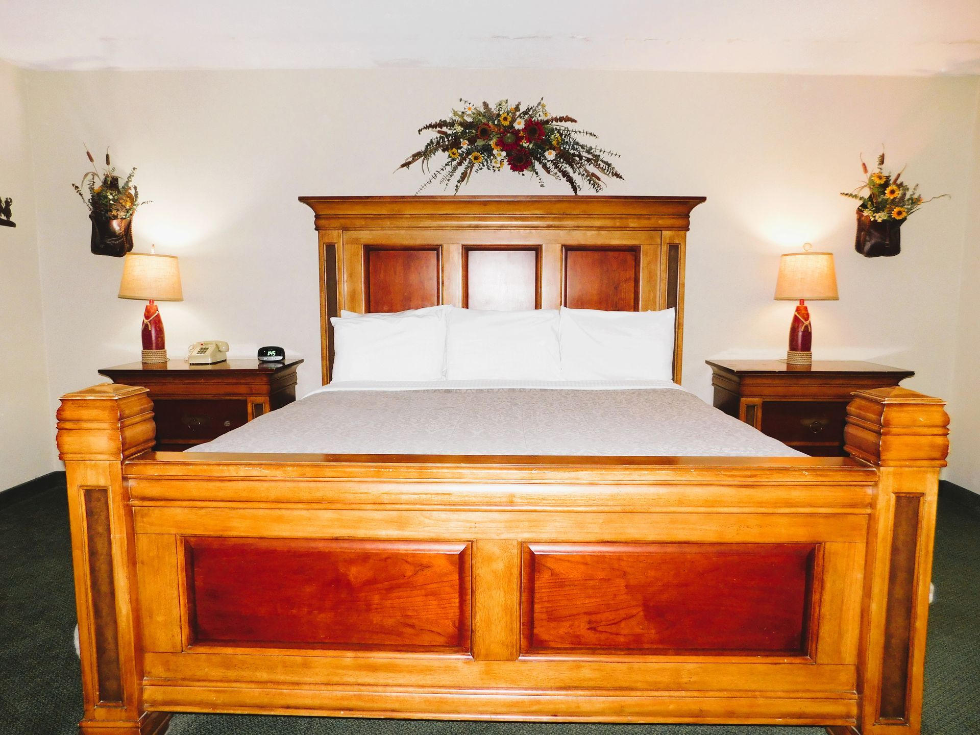 Wooden bed with nightstands, lamps, floral decorations, and a telephone in a hotel room.