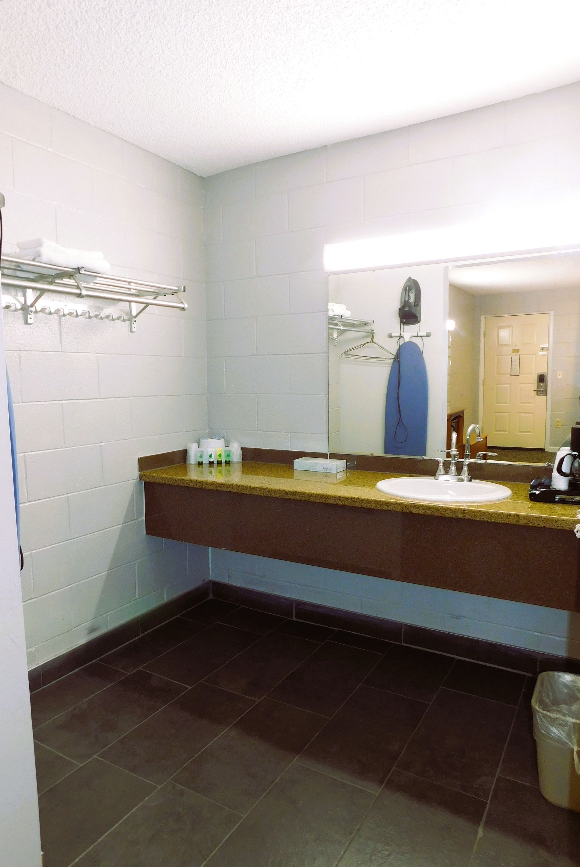 Bathroom with brown tiled floor, light walls, a long wooden vanity with a white sink, and a large mirror.