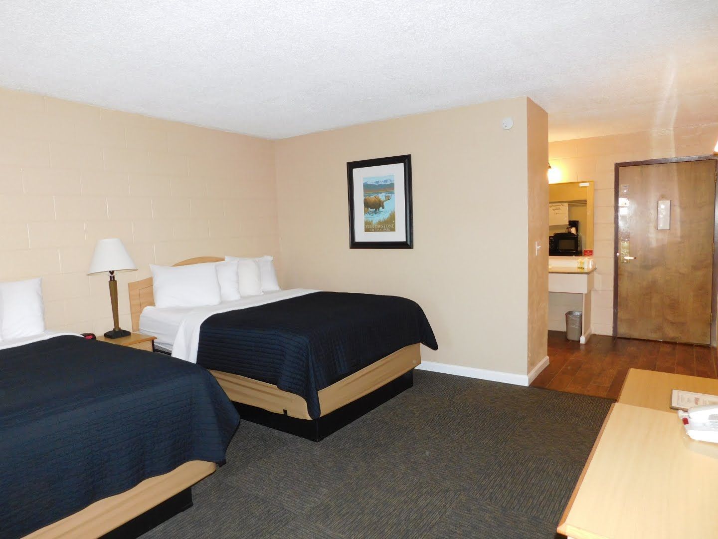 Hotel room with two beds, beige walls, a bathroom entrance, and a table.