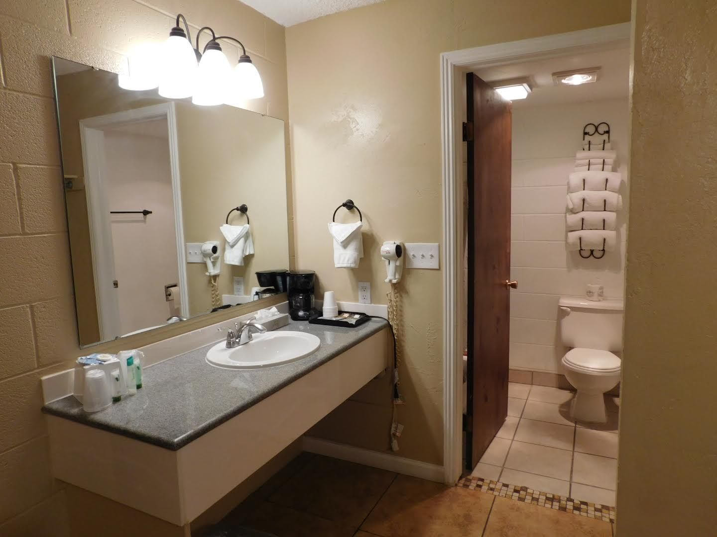 Bathroom with sink, mirror, and open doorway to toilet area. Beige walls, coffee maker on counter.