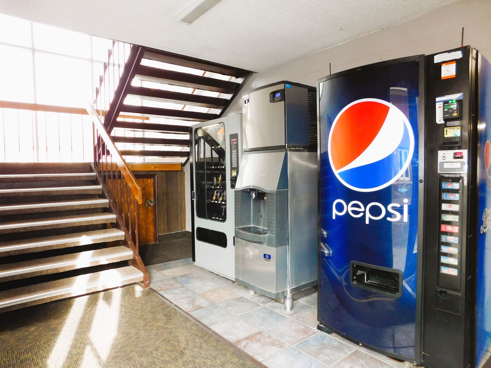 Vending machines and water dispenser next to staircase in a building. Pepsi logo prominent.
