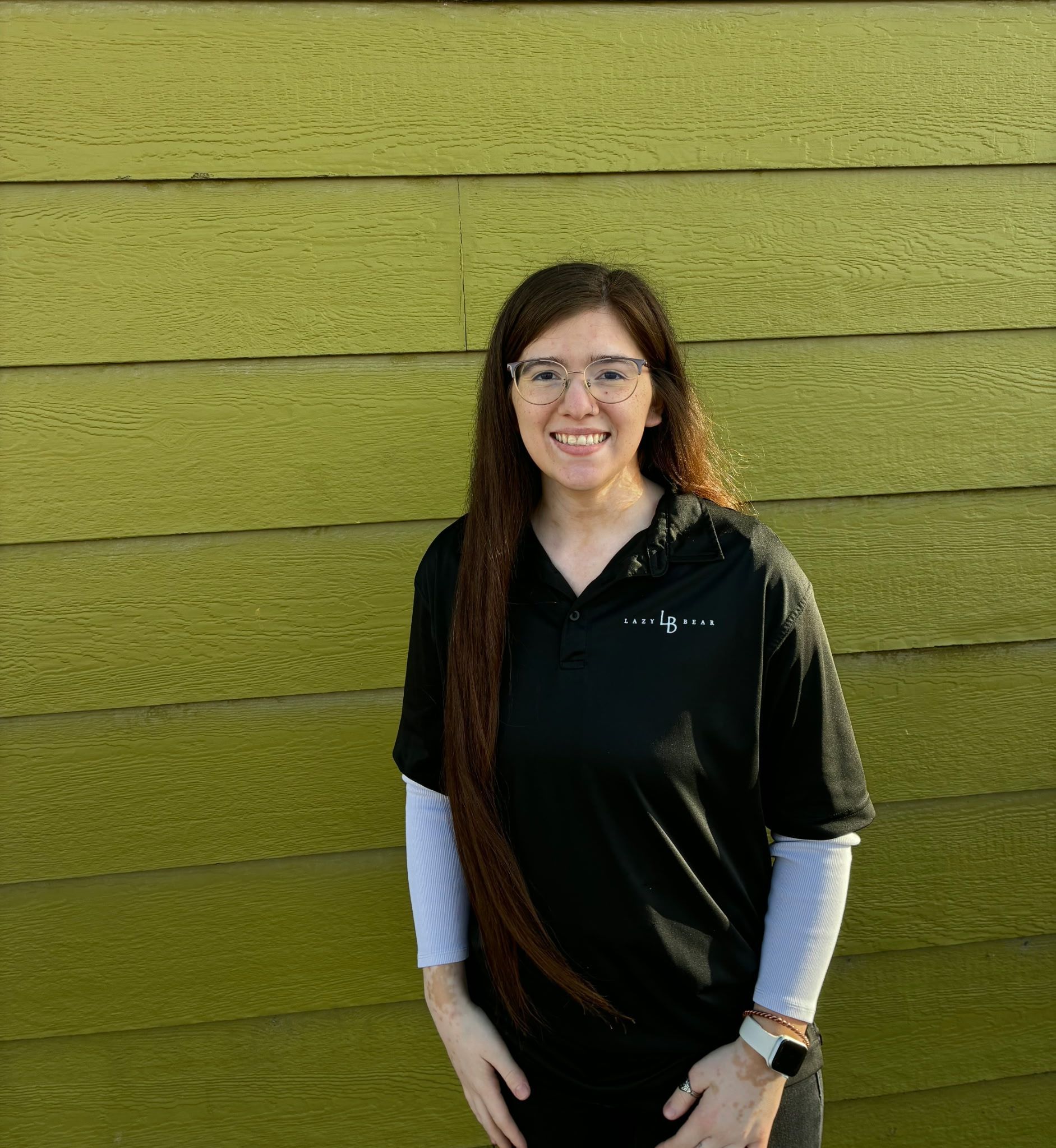 Woman standing outdoors in front of a green textured wall, smiling at the camera.