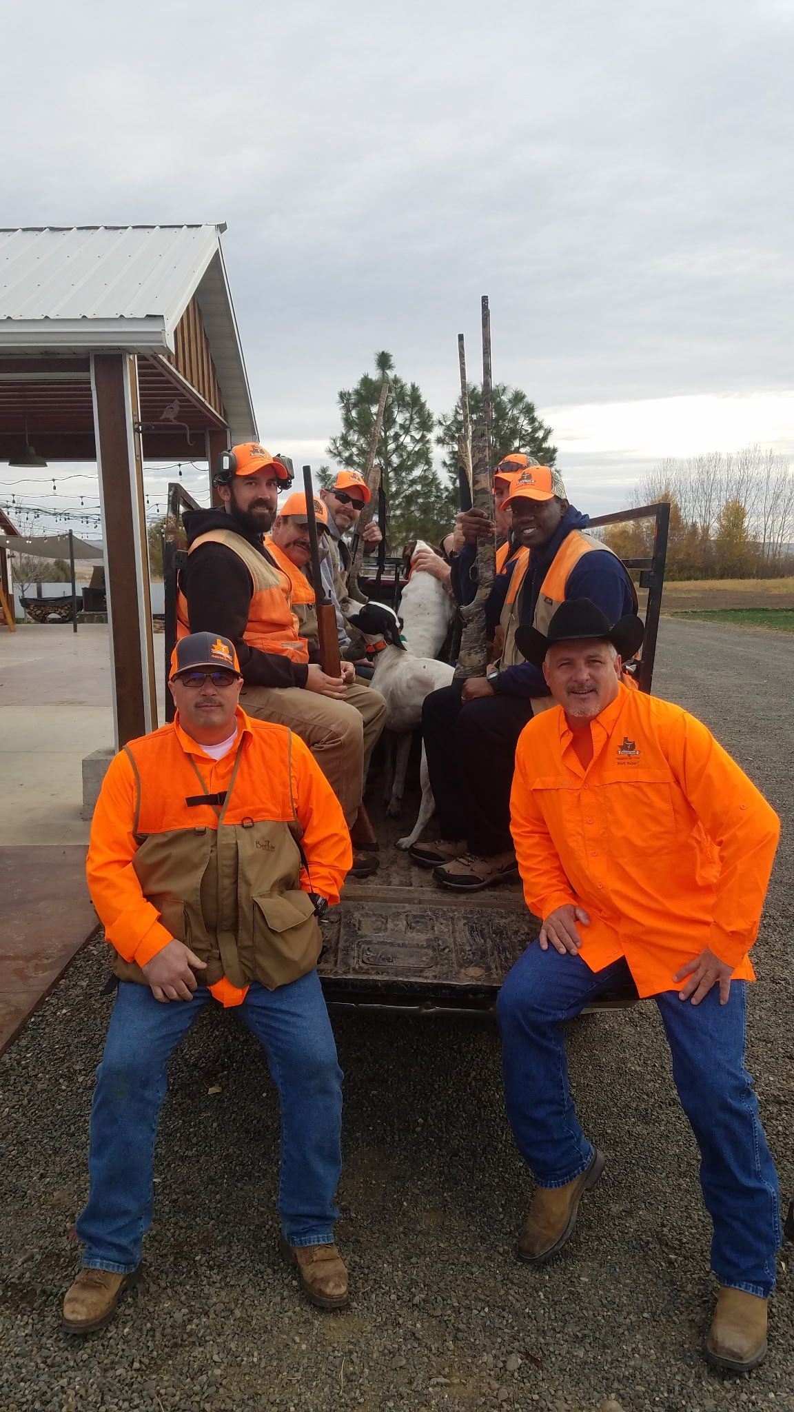 A group of people wearing bright orange hunting gear sitting on a trailer outdoors.