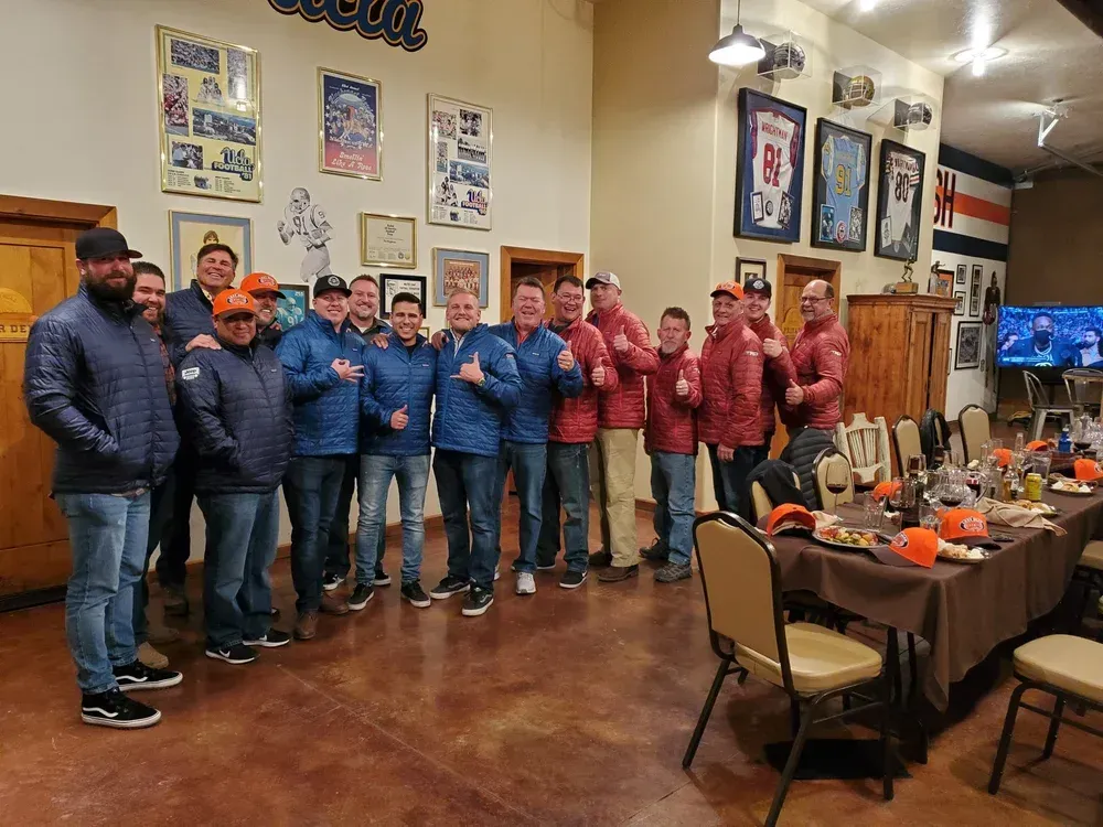 A group of people wearing blue jackets stand together in a restaurant with framed memorabilia on the walls.