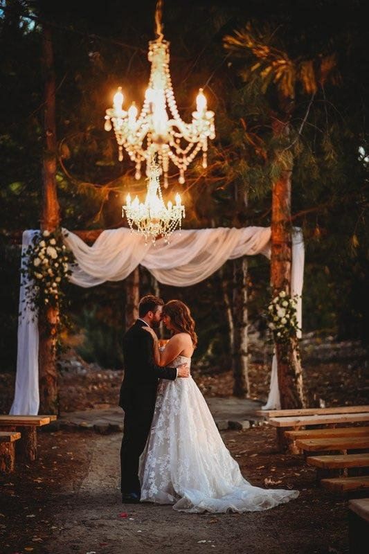 A couple in wedding attire sitting together on a wooden pier overlooking a calm lake at sunset.