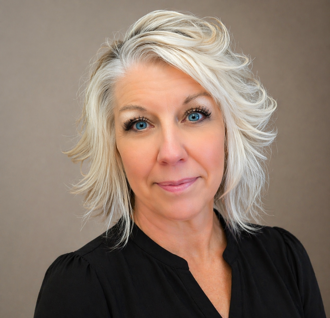 Portrait of a person with short silver hair, wearing a black top, against a plain beige background