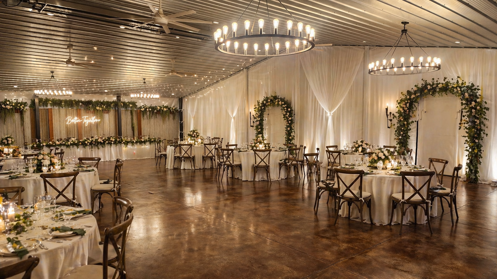 Elegant banquet hall with round tables, chandeliers, draped white curtains, and floral arch decorations