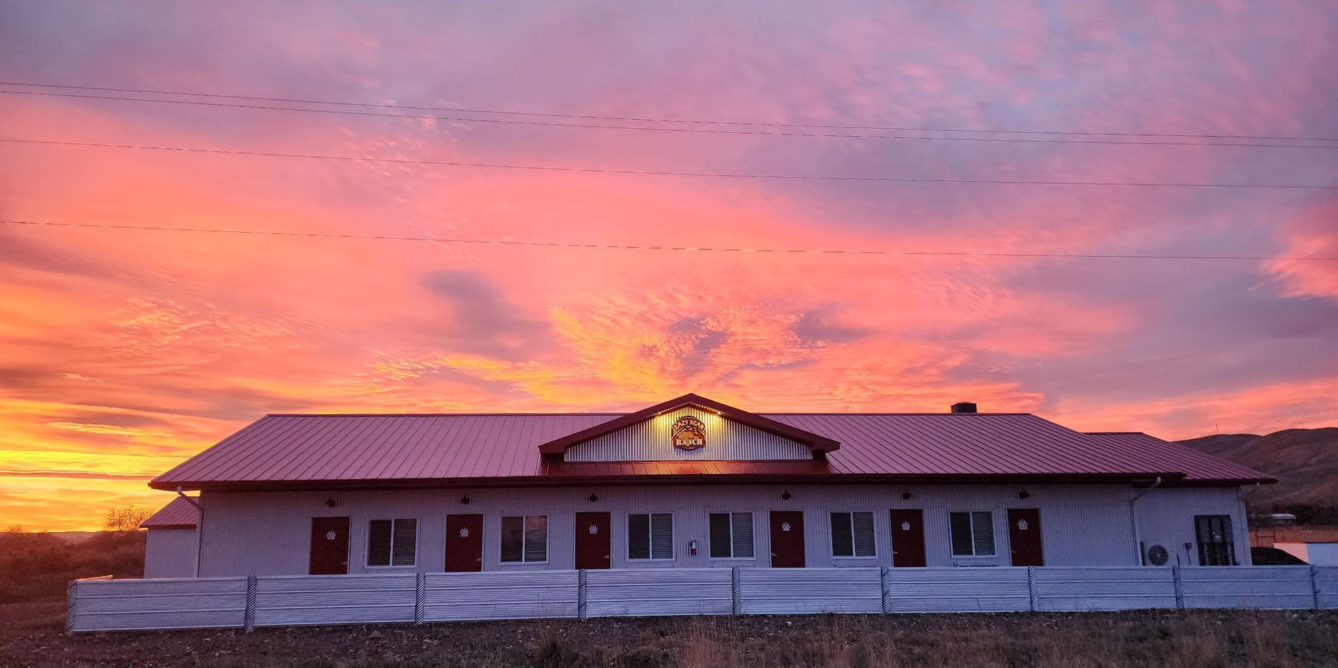 A low-slung, single-story lodge with a reddish roof against a vibrant pink and orange sunset over a rocky landscape.
