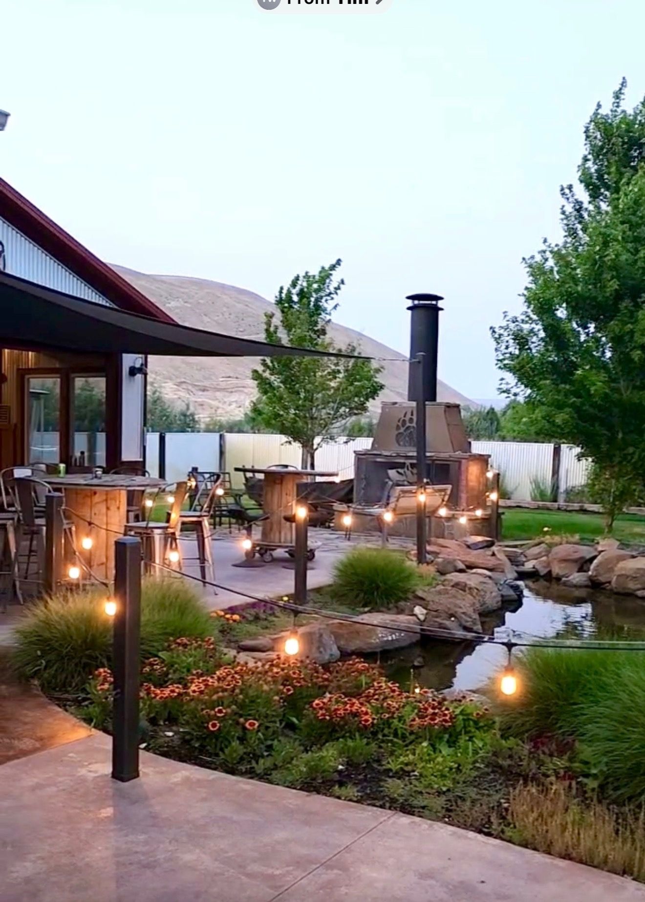 A covered outdoor patio featuring stamped concrete, string lights, and a view of a landscaped garden with a rock pond.