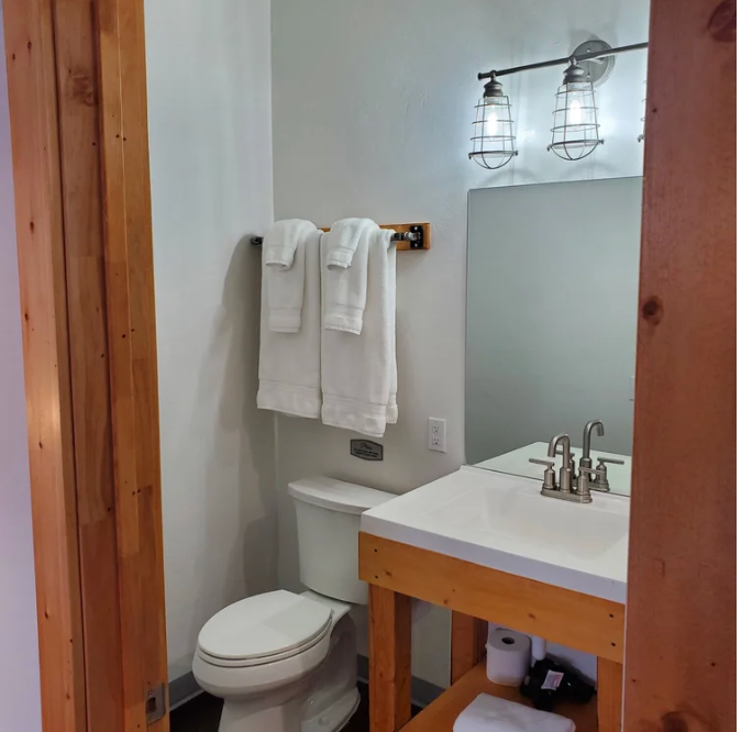 A bathroom with a white toilet, a wooden vanity with a white sink, a mirror, and white towels hanging on a wall rack.