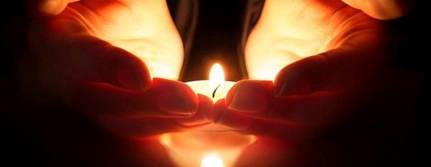 A person is holding a lit candle in their hands.