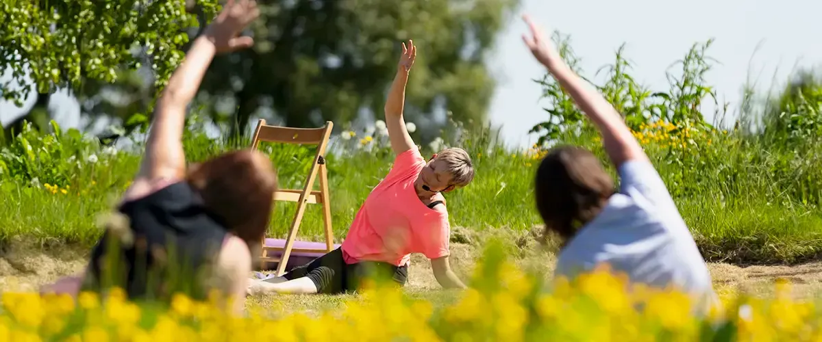 People seated in meadow with legs outstretched, practicing easy side stretches.