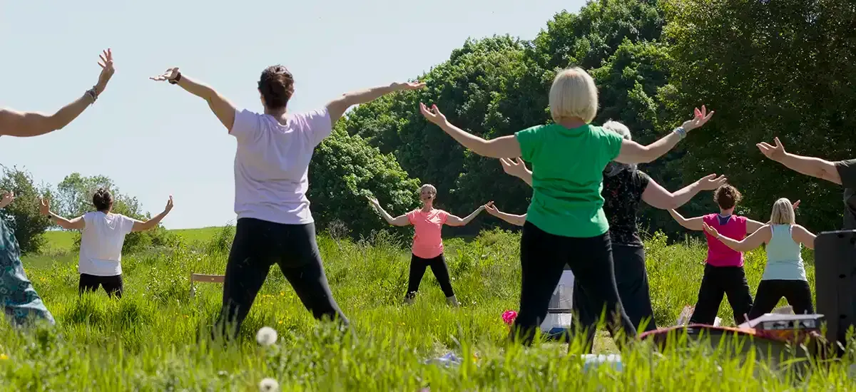 People standing in grass with upturned arms, practicing heart-opening yoga postures.