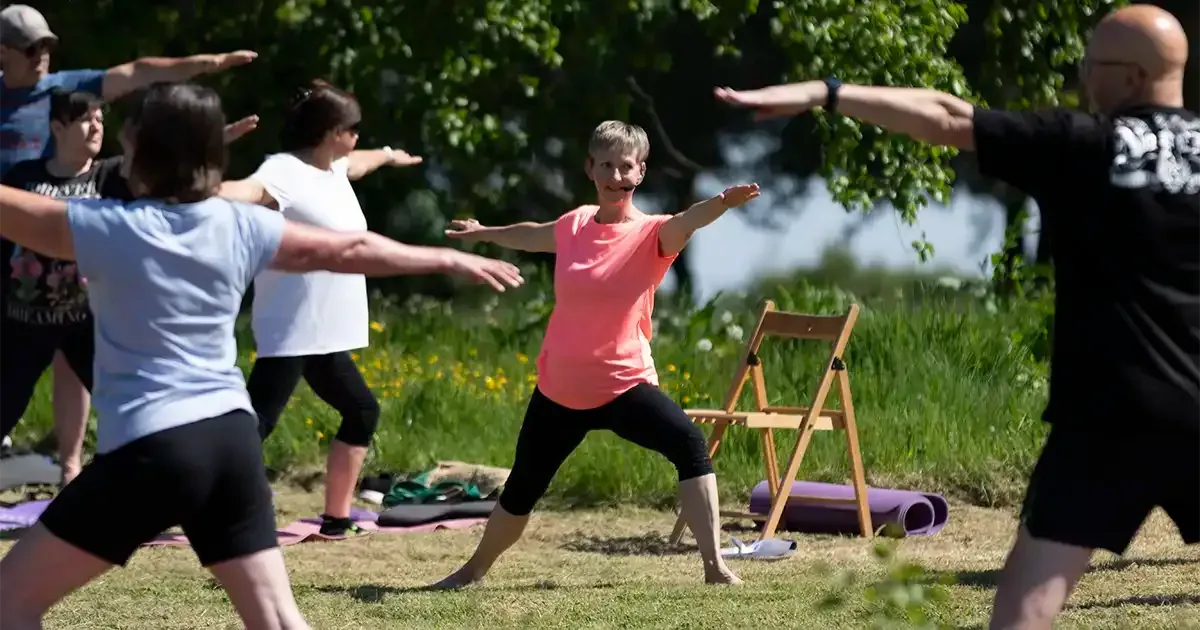 A yoga teacher demonstrating the warrior pose to a group of people practicing yoga outdoors.