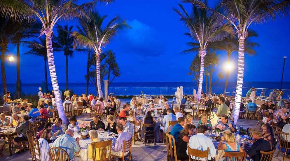 A large group of people are sitting at tables on the beach at night.