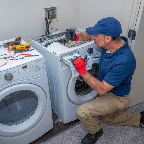 A man is working on a washing machine in a laundry room.