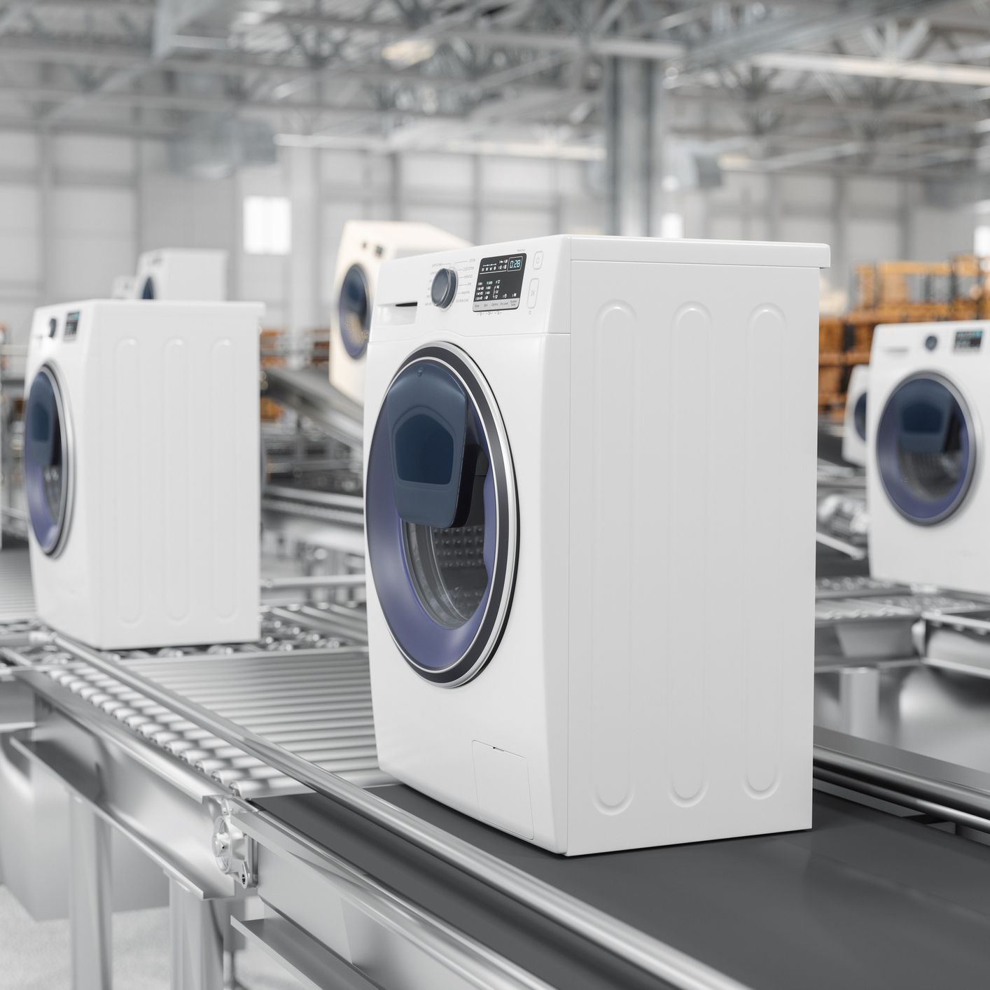 Three white washing machines are sitting on a conveyor belt in a factory.