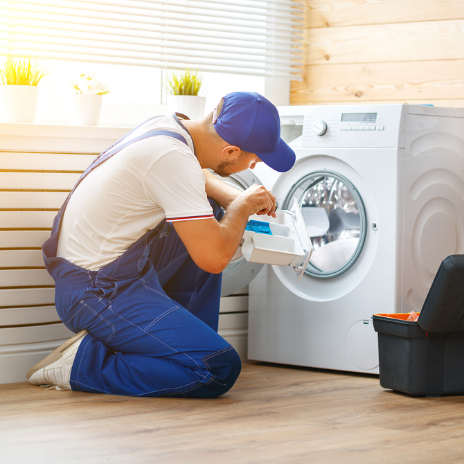 A man is kneeling down in front of a washing machine.